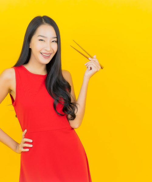 Portrait beautiful young asian woman with chopstick ready to eat on yellow background